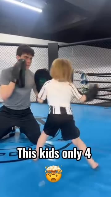 Tom Brennan on his knees holding focus pads for a young child in the cage.
