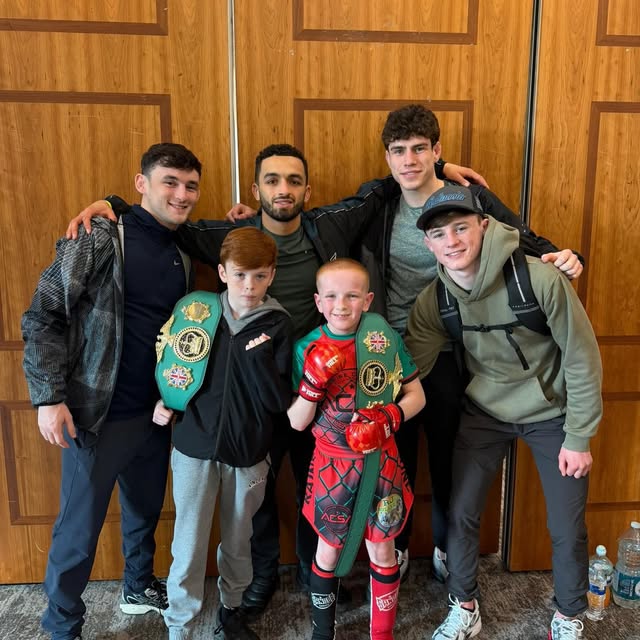 Two young fighters holding British title belts alongside their coaches after a competition.