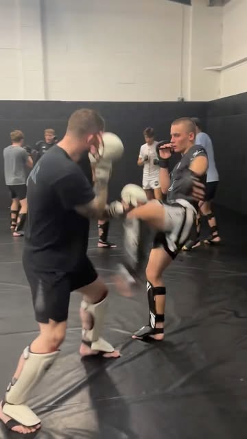 A beginners MMA class working kicks in pairs on the mats.